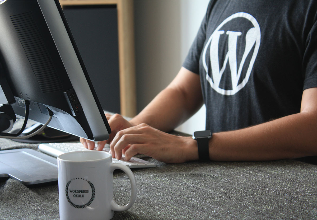 A person with a WordPress T-Shirt and mug typing at their screen.